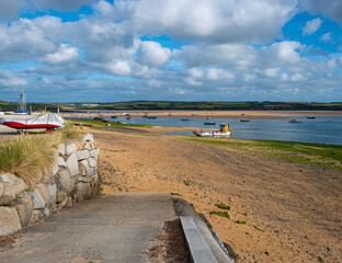 A ramp runs onto a sandy beach, beside the River Camel estuary at the coastal fishing village of Rock, opposite Padstow, in Cornwall, UK. Sailing boats. Cloudy blue sky.