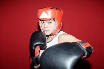 Young serious female boxer hitting her rival by left hand in boxing glove and keeping defense by...