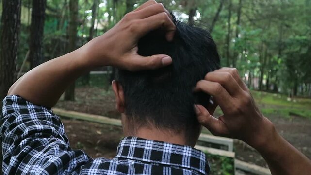 man scratching his head at park because of itchy dandruff
