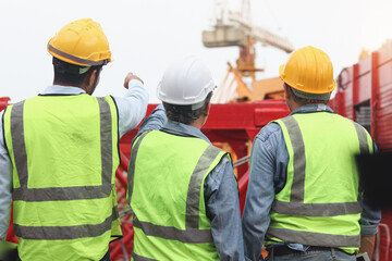 Group of engineer workers with safety vest and helmet from behind standing at construction building site. Architect team working together at workplace. Back of constructer at building site.