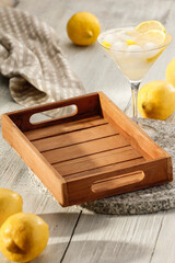 Water with lemon and ice cubes in cocktail glass, mocktail and lemons scattered on wooden table. Copy space for products.