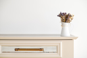 A bouquet of autumn asters in a white vase on a white chest of drawers.