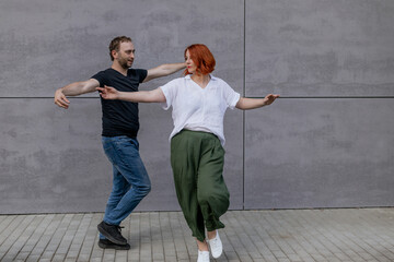 Happy dancers curling in dance in city. Romantic couple, woman with red hair and man in dark...