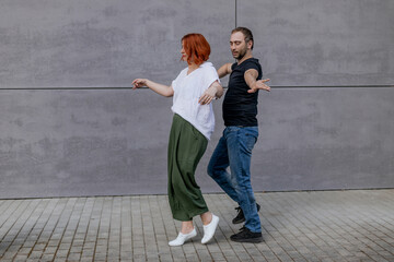 Happy dancers curling in dance in city. Romantic couple, woman with red hair and man in dark...