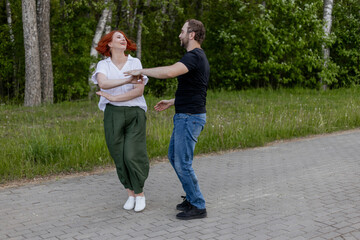 Happy dancers curling in dance in park. Romantic couple, woman with red hair and man in dark...
