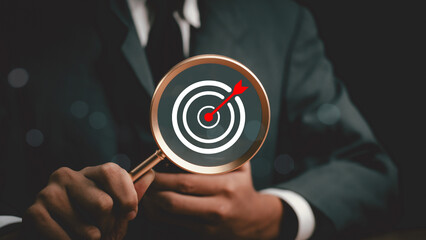 Man hold Target board inside of magnifier glass for focus business objective achievement concept. Search, goal, strategy, success.