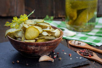 Bowl of tasty pickled cucumbers with spices and dill on wooden background. Marinated homemade...