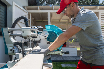 Carpenter Using Miter Saw to Cut Wood Planks Outdoors During Daytime