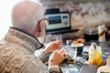 Elderly Man Enjoys Morning Coffee While Working at Home Office With Laptop