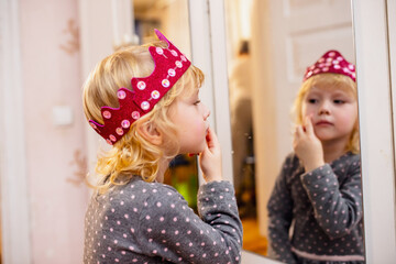 Young Child in Polka Dot Dress and Crown Examining Reflection in Mirror at Home