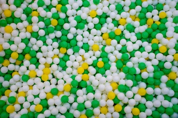 Top view of Beautiful colorful plastic balls in the playground background, Texture of multi colored balls of green, yellow and white. Swimming pool with colored Balls.