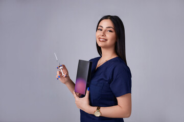 Fototapeta premium Portrait of an American beautiful female cosmetologist doctor in a white coat with an injection syringe. Medical student. Female hospital worker looking at camera and smiling, studio, gray background