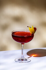 New Yorker cocktail with whiskey, grenadine, bitters, lemon juice and ice, garnished with lemon zest and cherries in glass. Beige background, hard light