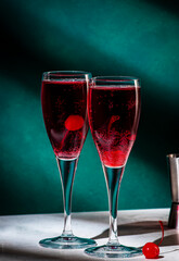 Red alcoholic cocktail drink with black currant liqueur, sparkling wine and cherry. Dark green background