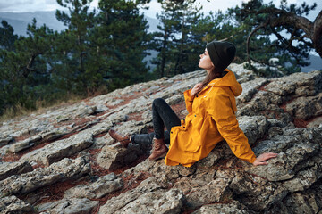 A woman in a vibrant yellow jacket enjoying the breathtaking view from the top of a mountain surrounded by lush trees