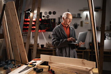 Male Woodworker Using Laptop Computer. male Carpenter Working in a Studio with a lot of Tools on the Walls.