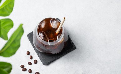 Coffee espresso in a glass with ice on a black board on a light background with coffee beans and leaf.