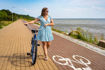 Summertime activity. Beautiful woman with long blond hair wearing blue dress walking with blue...