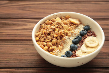 Oat raisin granola with fresh summer berries in a bowl on brown wooden background. Concept of healthy breakfast food, clean eating, dieting