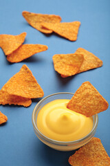Tasty nachos with cheese sauce on blue background. Vertical photo