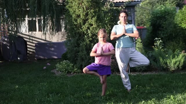 mom and child daughter do yoga in the summer garden near the house. Healthy lifestyle concept. solo outdoor activities. practice Tai Chi Chuan