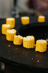 Grilled cut corn cobs on round stove with open fire outdoors, event cooking.