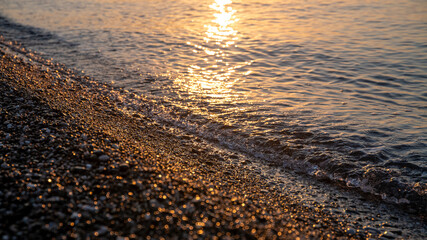 sea surf on a pebble beach, at sunset or sunrise, summer natural background, rest and relaxation by the sea