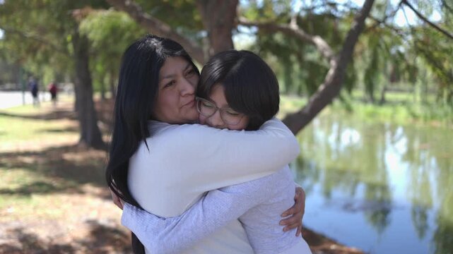 Mexican mother hugging her teenage daughter at the park, mothers day concept