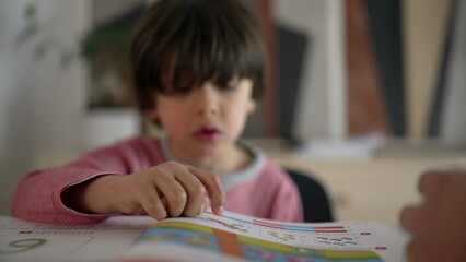 Close-up of child reading a colorful book with parental guidance, highlighting concentration and the joy of learning in a supportive home environment