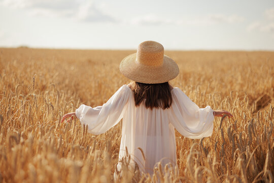 Woman in wheat field wearing straw hat, cereal crop cultivation concept