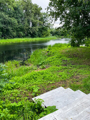 A picturesque river, gracefully surrounded by lush trees and vibrant grass, with a set of inviting stairs leading down to its tranquil waters, creating a perfect natural landscape