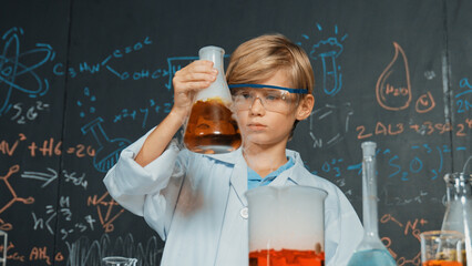 Smart boy inspect mixed chemical liquid in laboratory beakers while holding and looking carefully. Caucasian child focus on doing an experiment in chemistry lesson or STEM science class. Erudition.