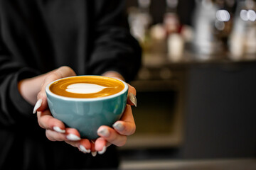 person holding ceramic cup with intricate latte art, showcasing heart design on the coffee’s surface. image captures cozy, inviting atmosphere, perfect for promoting coffee culture or café experiences