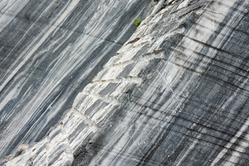 Close-up of a wall of black-grey marble in a quarry. There is a foreground and background, traces of sawing and drilling. Background.
