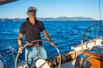 Fototapeta premium Young man captain stands at the helm and controls a sailboat during a journey by sea