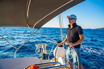 Young man captain stands at the helm and controls a sailboat during a journey by sea