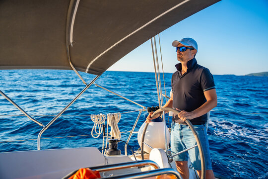 Young man captain stands at the helm and controls a sailboat during a journey by sea