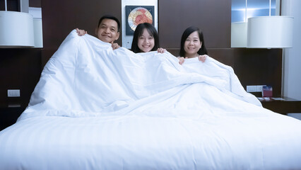 Parents and daughter prepare to rest on a large bed in a luxury hotel. The family enjoys a relaxing holiday in the hotel.