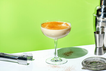 Beige creamy cocktail drink with cognac, liquor, nutmeg and ice. on green background, hard light