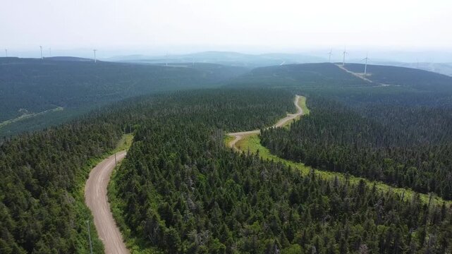 Ascension a&eacute;rienne verticale a vue de drone au-dessus de chemins forestiers parcourant le site d'&eacute;oliennes du Lac Alfred, Monts Chics-Chocs, Qu&eacute;bec sur des montagnes enfum&eacute;es a perte de vue. 