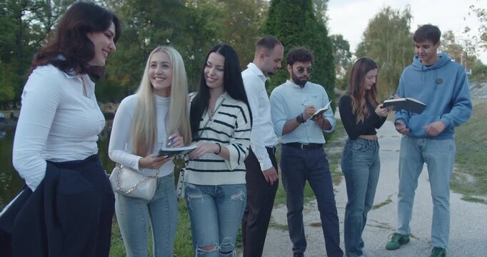 A multicultural group of university students chats and enjoys the outdoors in a park, possibly discussing classwork or life.