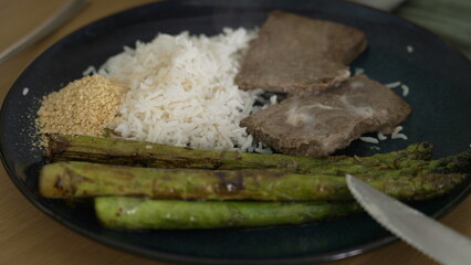 Plate with grilled asparagus, steamed white rice, tender steak, and a side of crushed garlic, perfect for showcasing a balanced and nutritious meal in food photography and culinary presentations