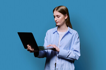 Smiling teenage girl with laptop on blue studio background