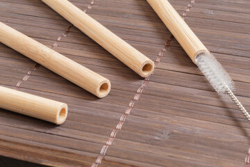 Close-up of four bamboo straws on a bamboo table, one of the straws has a cleaning brush inserted. Concept of environmental conservation and hygiene. Reusable products.