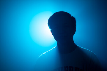 Silhouette of a man in a dark environment, illuminated by a blue backlight. The figure appears...