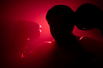 A silhouette of a boxer in gloves flexing his muscles against a dramatic red and blue background. The contrasting colors create a powerful and intense atmosphere, highlighting the strength