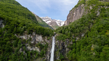 Majestic Waterfall Cascading Down Rocky Cliff Surrounded by Lush Green Forests and Snow-Capped Mountains at Sunrise