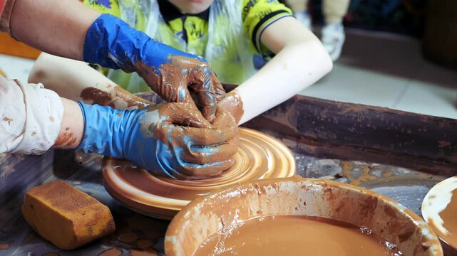 Close-up of children's hands sculpting ceramic dishes from clay in the workshop.
