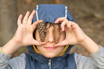 Smiling boy in a blue hooded jacket holding pine cones, enjoying a day in nature. Concept: Showcasing the importance of connecting children with nature to inspire environmental stewardship and