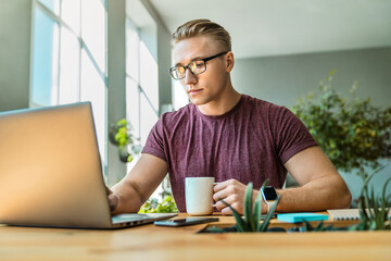 Male executive worker sitting in office with cup of coffee and working on notebook. Young...